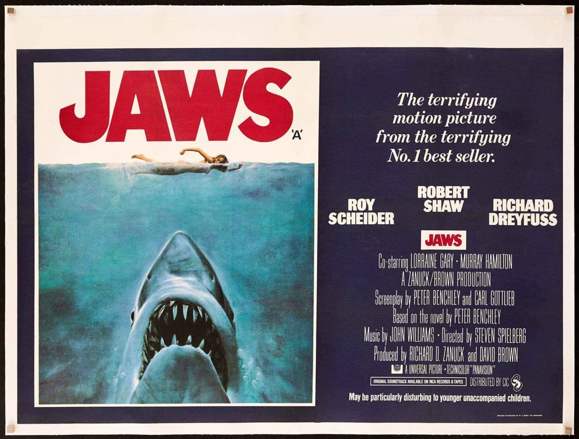 The 1975 Jaws poster contrasts a swimmer on the surface with an enormous shark rising below.